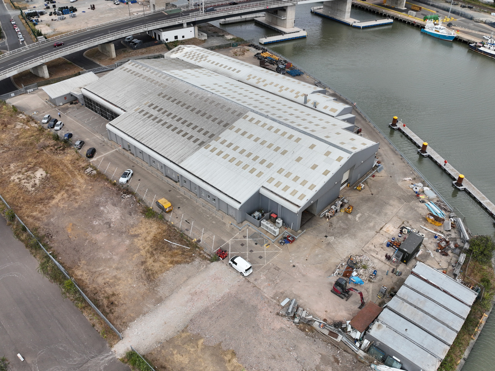 Aerial view of an industrial waterfront site showing the building, yard, quay, water and bridge together.